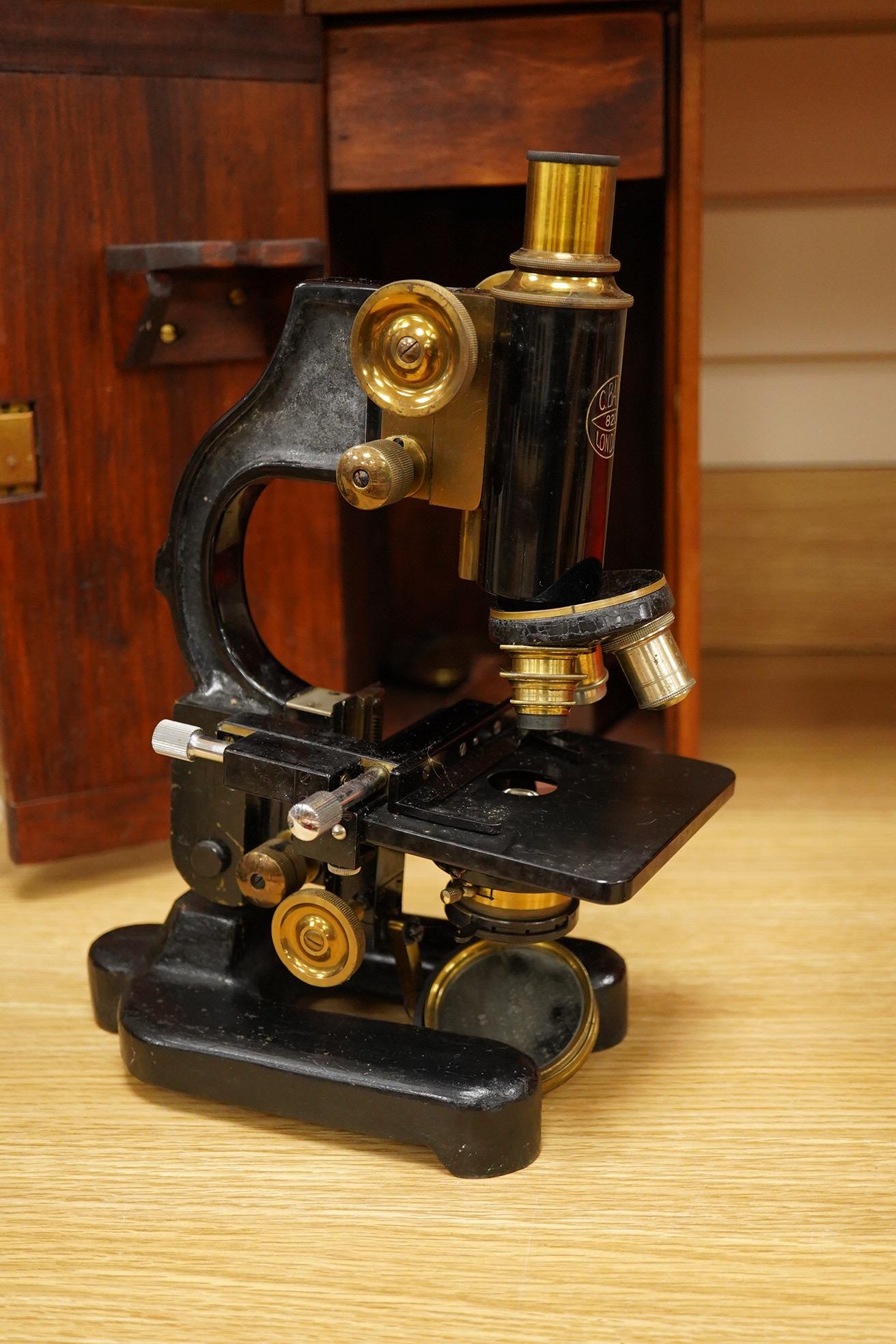 An early 20th century pine and plywood cased microscope by C.Baker, London, containing an integral drawer with alternative lenses, and a magnifying glass on a brass stand, the case dimensions; 38cm high, 18cm wide, 27.5c
